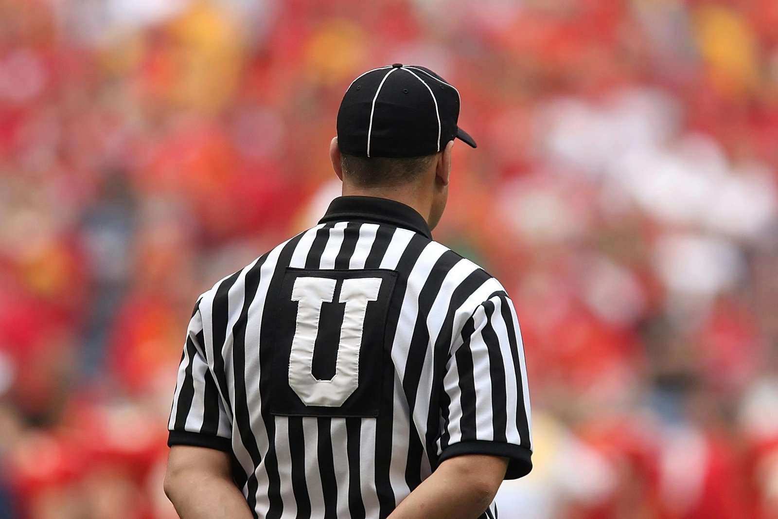 About 3 A football umpire in uniform overseeing the game in a crowded stadium.