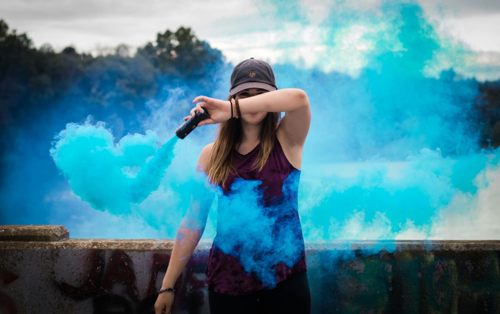 Home 6 A stylish woman surrounded by bright blue smoke outdoors, creating a dynamic fashion statement.