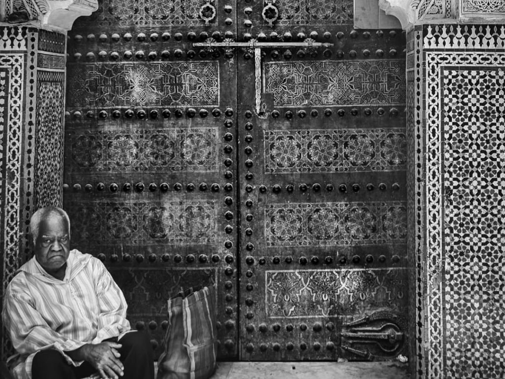 A vibrant scene in Fez El Bali (the old medina), showing a narrow alleyway with traditional shops and locals going about their daily lives. This image represents the authentic stories and cultural heritage of Fez as told by its people.
