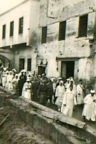 A historical image of King Mohammed V walking through the narrow alleys of Fez, accompanied by Moroccan and French guards. The scene symbolizes his deep connection with the people in the ancient city.