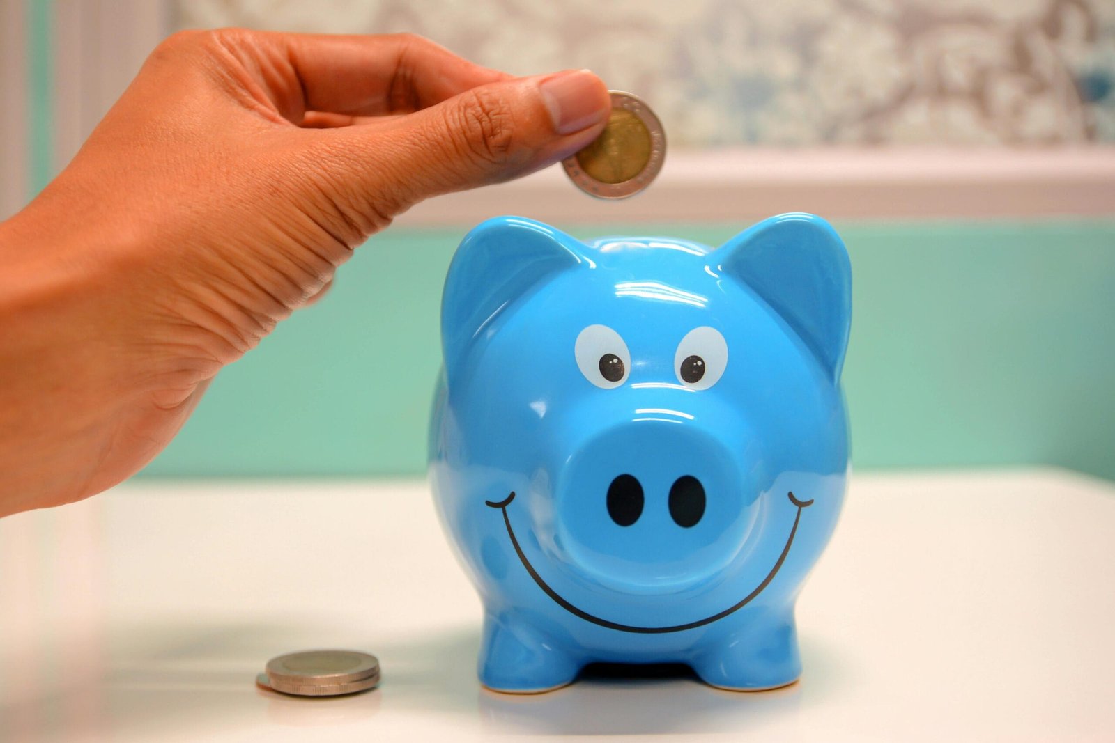 Airport Transfers 2 Hand inserting a coin into a blue piggy bank for savings and money management.