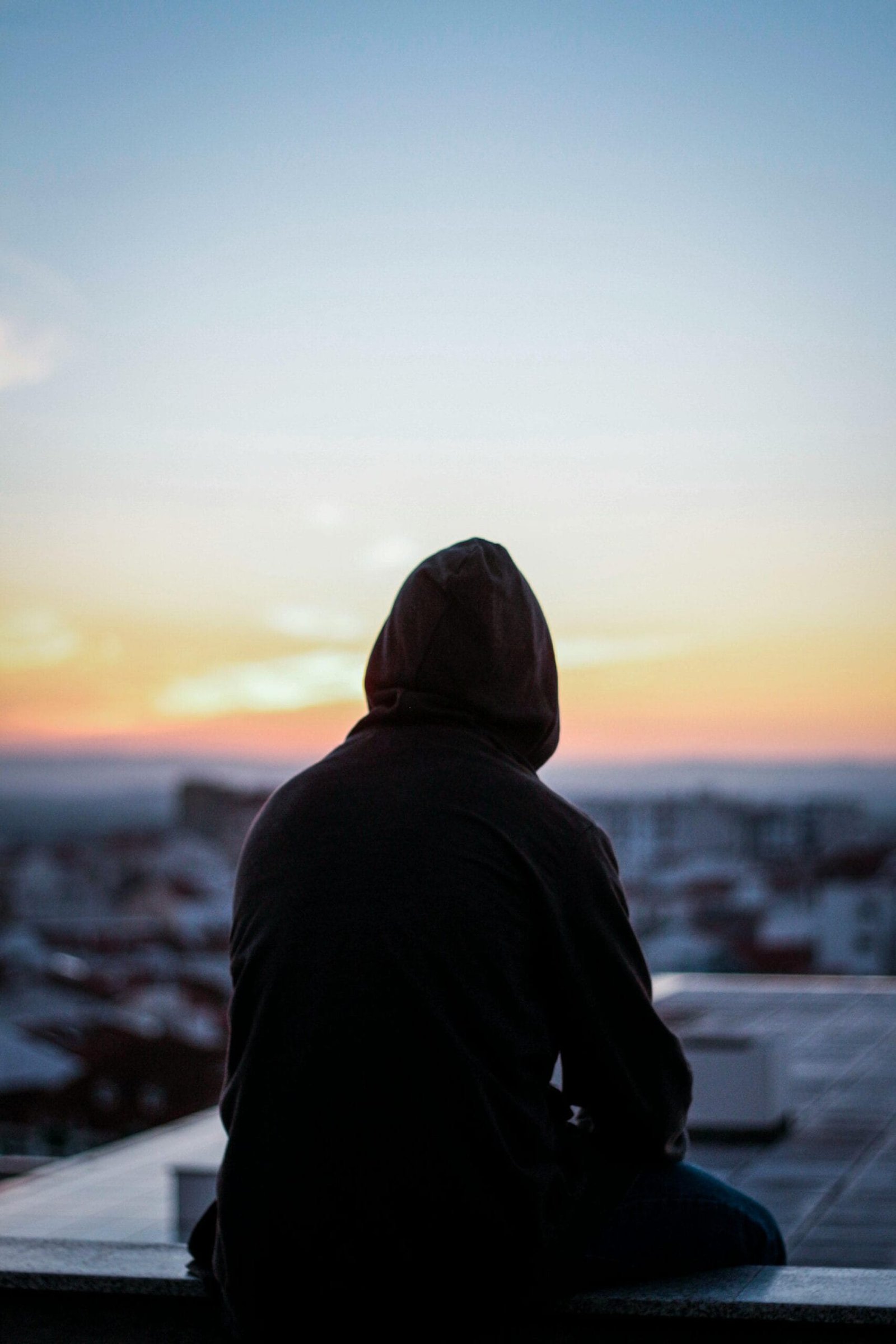 Airport Transfers 4 A solitary figure in a hoodie gazes at a vibrant sunset from a rooftop, creating a peaceful silhouette.
