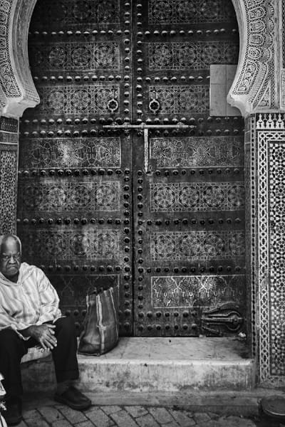 A person stands in contemplation before a richly decorated archway with intricate stucco and Zellige in a traditional Fez Zawiya. The scene captures the peaceful spiritual energy and architectural beauty of the Zawiya of Sidi Ahmed Tijani, a living piece of Morocco’s rich Sufi heritage.