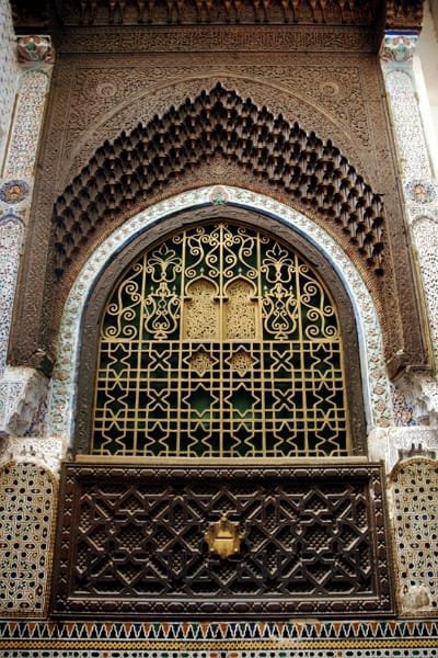 A beautiful view of a courtyard or archway decorated with intricate Moroccan Zellige tilework, symbolizing the serene and spiritual architecture of the Sidi Ahmed Tijani Mausoleum in Fez. The site is a key religious complex for the Tijaniyya Sufi order.