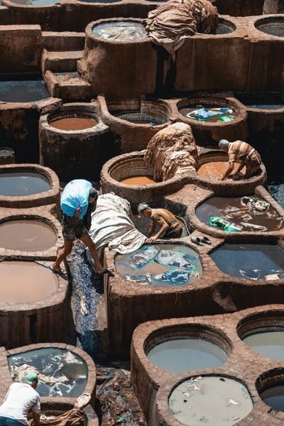 A wide, panoramic view of the Chouara Tannery in Fez, showcasing the vast complex of traditional dye and treatment pits and surrounding buildings. This iconic site is the oldest tannery in Fez, offering a glimpse into a thousand years of unchanged Moroccan leather crafting traditions.