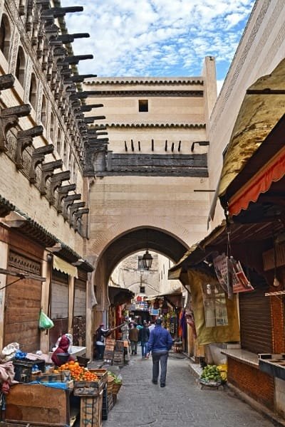 A tourist with a backpack safely walking through a narrow, arched street in the heart of the Fez Medina. This image reinforces the message that Fez is an excellent and secure tourist destination known for its historical charm.