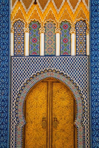 A magnificent close-up of the Royal Palace of Fez's golden gate, decorated with blue zellige tiles and ornate golden stucco, representing the stunning royal architecture and history of Fez.