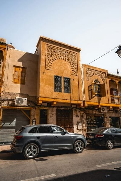 A street view in the historic Jewish Mellah of Fez, showcasing a building with distinct architecture, including ornate carved plasterwork and wooden windows. This area highlights the Jewish heritage adjacent to the Royal Palace.