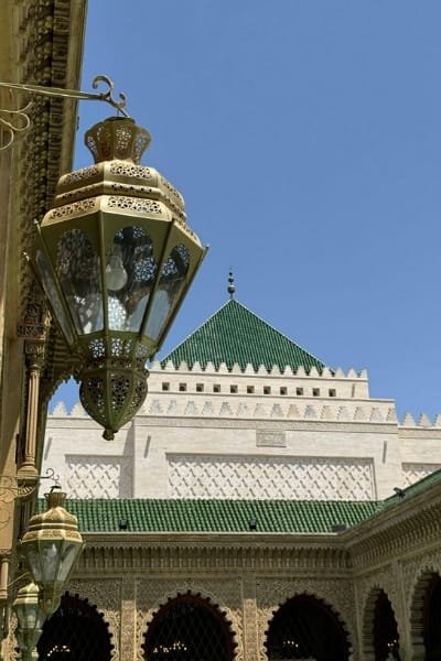 A close-up of the magnificent gate of the Royal Palace in Fez, showcasing intricate deep blue and white zellige tilework surrounding a horseshoe arch. The detail highlights the luxury and majesty of the royal architecture.