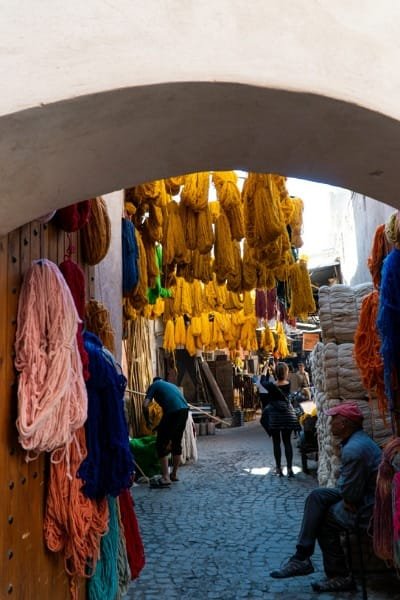View through a Moroccan archway into the Souk as-Sabbaghine (Dyers' Quarter) in Fez, showing abundant bright yellow and colorful hand-dyed yarns hanging overhead. This scene highlights the traditional artisanal skills and natural dyes.