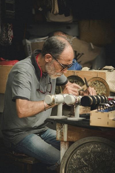 A skilled Moroccan artisan in Fez focused on the intricate hand-engraving of brass bangles. This traditional process transforms raw metal into exquisite functional art, often featuring geometric and floral motifs.