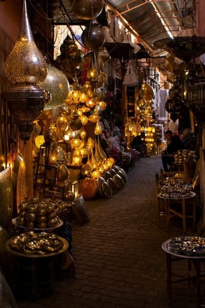 A narrow alley in Fez's metal souk, illuminated by numerous shining brass and copper lanterns. These exquisitely crafted metal pieces showcase the precision and patience of Moroccan engraving artisans.