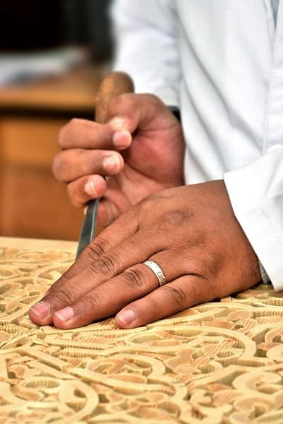 Prepare to be enchanted by the exquisite artistry of wood carving in Fez, a craft deeply ingrained in Moroccan tradition and rich with symbolism. Here, master woodcarvers possess the remarkable ability to transform the fragrant, unassuming wood of the cedar tree into breathtaking displays of intricate, hand-carved geometric patterns and flowing arabesque motifs. These stunning creations grace the architectural elements of Fez, adorning majestic doors that invite you into hidden worlds, grand ceilings that inspire awe, delicate window screens that filter the light in mesmerizing ways, and elegant traditional Moroccan furniture that speaks of heritage and comfort. This delicate art is not acquired overnight; it demands years of rigorous training, a keen eye for the smallest detail, and an innate artistic sensibility. Each carved panel is more than just decoration; it whispers a story, reflecting the profound spiritual harmony, the elegant balance of mathematical principles, and the deep-seated aesthetics of Islamic art. Whether you find it adorning the sacred space of a mosque, the opulent halls of a palace, or the tranquil ambiance of a traditional riad, the presence of meticulously carved woodwork invariably adds a layer of warmth, beauty, and profound cultural significance to every space it graces. The magic of Fez's wood carving lies in several key aspects: A Legacy of Timeless Skill: Every single piece is a testament to human artistry, carved entirely by hand. Using what appear to be simple tools, these artisans draw upon an immense reservoir of knowledge and experience passed down through generations, transforming raw material into intricate beauty. A Symbol of Prestige and Refinement: In Moroccan culture, the presence of fine woodwork is often associated with nobility, elegance, and a deep appreciation for refined aesthetics. It speaks of heritage, taste, and a connection to the rich artistic traditions of the land. A Living Act of Cultural Preservation: The continuation of this exquisite tradition is a testament to the dedication of the artisans who tirelessly keep this art form alive. Through the vital practice of master passing their knowledge and skills to apprentice, the legacy of Moroccan wood carving endures, ensuring its survival for generations to come. As you explore Fez, take a moment to truly appreciate the artistry of the woodcarvers. Their work is a tangible expression of the city's soul, a beautiful reminder of the enduring power of human skill and the timeless elegance of Moroccan artistic heritage.