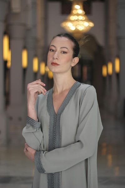 A model wearing an elegant grey Moroccan caftan adorned with intricate Fez silk embroidery. The fine detail and delicate stitches showcase the craftsmanship perfected in Fez for generations.
