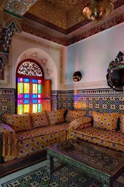 A luxurious Moroccan salon interior in Fez featuring large seating areas covered in fabric with intricate Fez embroidery. The silk embroidery, known for its precision, adds a touch of tradition and elegance to the home furnishings.