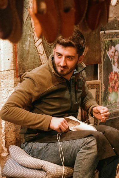 A young Khraaz artisan in Fez meticulously hand-stitching a traditional Moroccan Balgha slipper using high-quality leather. This craft is an authentic cultural experience found in Qasaria al-Kifah and showcases the detailed work required for this iconic footwear.