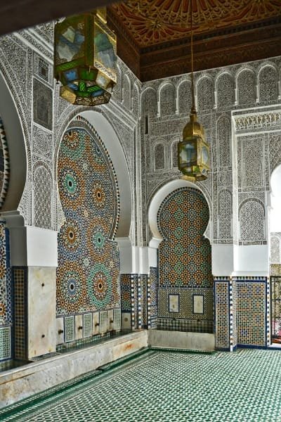 The richly decorated interior of a spiritual lodge in Fez (representing Sheik Ahmed Al Tijani Zawiya), featuring intricate Zellige mosaic tiles, traditional archways, and gypsum carvings. The Zawiya is one of the most important spiritual lodges in the city.