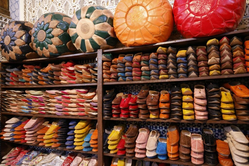 Fez Shopping Guide: What to Buy in Morocco’s Craft Capital 4 In the vibrant streets of Fez, one of the most notable traditional crafts is cobbling, where artisans craft the iconic Moroccan footwear that has become a symbol of the country’s rich cultural heritage. The artisans, known as khrazz (cobblers), specialize in creating a variety of handmade leather shoes such as belgha (traditional Moroccan slippers) and chebbel (slip-on leather shoes). 👟 What You’ll Find: Belgha (Moroccan Slippers) The most famous of Moroccan footwear, belgha is made from high-quality leather and is often characterized by its pointed toe and soft feel. These slippers are not only stylish but are also comfortable and versatile, making them perfect for both casual and formal wear. Chebbel Similar to the belgha but with a more refined design, chebbel shoes are often embroidered and are considered more formal. They are ideal for special occasions or daily use, depending on the style chosen. 🏛️ Where to Find It: The craft of the cobbler is thriving in Kasaria El Kifah, located in the heart of Fez’s medina, especially near Csaria El Attarine. Here, artisans are busy crafting these timeless shoes by hand, using traditional techniques passed down through generations. The market is a hub of leather goods, with numerous shops selling handmade shoes, providing visitors with a chance to purchase unique, high-quality footwear. 🌟 Why It’s Worth Visiting: Handcrafted Heritage: Each pair of shoes is created with attention to detail and is made to last, showcasing the deep knowledge of Moroccan craftsmanship. Authenticity: The shoes sold in this market are authentic, hand-made by local artisans who take pride in preserving their craft. Perfect Souvenirs: Moroccan leather shoes are popular souvenirs for travelers, thanks to their unique style and durability. Tip for visitors: Visit the workshops in Kasaria El Kifah, where you can watch khrazz artisans at work and purchase a pair of belgha or chebbel to take home as a piece of Moroccan culture.
