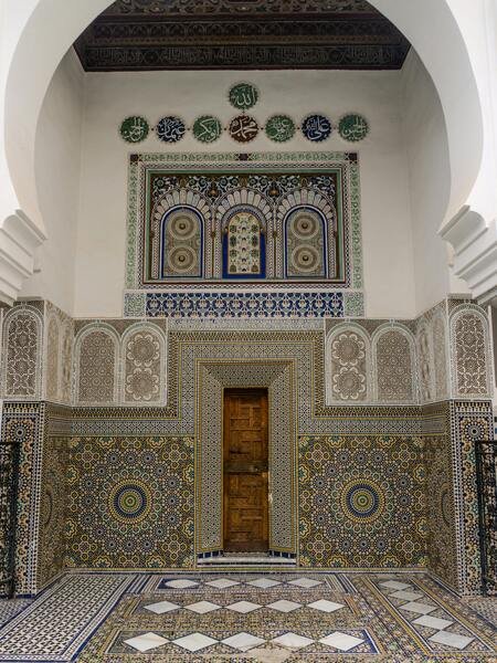 A female tourist standing in an exquisitely decorated Fez courtyard featuring Zellige tiles and carved stucco. This image captures the beauty of Fez, a secure tourist city that welcomes visitors to explore its rich architectural heritage.
