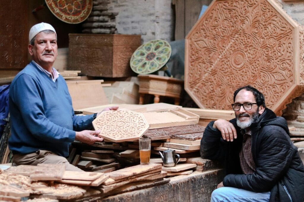 Top Things That Make Fez Special: History & Handicrafts 81 Prepare to be enchanted by the exquisite artistry of wood carving, a craft deeply ingrained in Moroccan tradition and held in particularly high esteem in the cultural heart of Fez. Here, master woodcarvers, with their skilled hands and keen eyes, transform the fragrant, unassuming cedarwood into breathtaking displays of intricate, hand-carved geometric patterns and flowing arabesque motifs. These stunning creations grace the very fabric of Fezzi architecture and design, adorning majestic doors that invite entry, soaring ceilings that inspire awe, delicate window screens that filter the light, and elegant pieces of traditional Moroccan furniture that add character and warmth to every space.Imagine the dedication and years of rigorous training required to master this delicate art. Each carved panel is a testament to the artisan's profound eye for detail and their deep understanding of the wood itself. More than mere decoration, each carving tells a silent story, reflecting the spiritual harmony, the mathematical balance, and the profound aesthetics that lie at the heart of Islamic art. Whether you find yourself within the serene ambiance of a mosque, the opulent halls of a palace, or the tranquil courtyard of a traditional riad, the presence of intricately carved woodwork adds an undeniable layer of warmth, beauty, and cultural richness to the atmosphere.The allure of Fez's wood carving tradition lies in several key aspects:A Legacy of Timeless Skill: Every exquisite piece is brought to life entirely by hand. Utilizing what might seem like simple tools, these artisans draw upon immense knowledge, hard-earned experience, and an innate understanding of their craft passed down through generations.
A Symbol of Prestige and Refinement: Within Moroccan culture, the presence of fine woodwork is often associated with nobility, elegance, and a deep sense of refinement. It speaks to a tradition of valuing artistry and craftsmanship in the highest regard.
A Living Act of Cultural Preservation: The continuation of this beautiful art form is a testament to the dedication of the artisans themselves. Through the time-honored tradition of master to apprentice, they ensure that this vital aspect of Moroccan heritage not only survives but continues to flourish, enriching the cultural landscape of Fez and beyond.
Allow yourself to be captivated by the silent eloquence of carved wood in Fez, a testament to the enduring power of human skill, artistic vision, and the profound beauty of tradition.