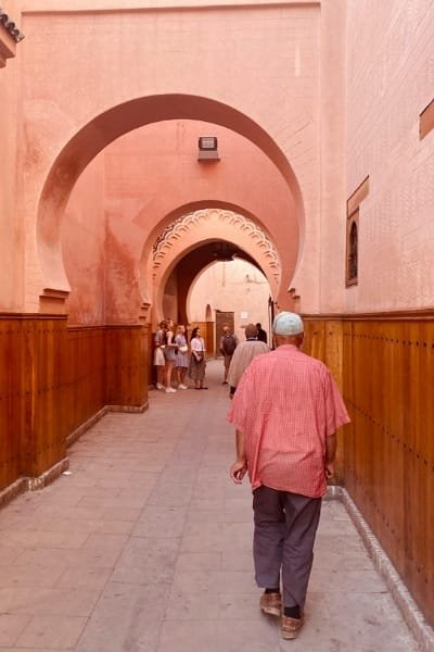 A towering minaret with green Zellige tiles rises above a narrow, bustling alleyway in the ancient Fez medina. This scene captures the essence of Fez, known for its deep spiritual heritage and intellectual legacy, with its maze-like rooftops and towering minarets.