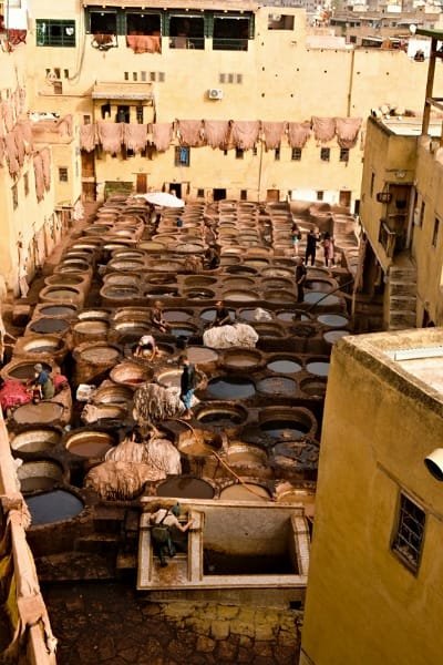 An overhead view of the Chouara Tanneries in Fez, showcasing the vast circular vats filled with colorful natural dyes. This image captures the authentic atmosphere of the largest and oldest leather tanneries in Morocco, where hides are treated using centuries-old traditional methods.