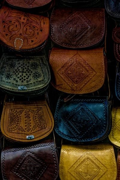 A close-up view of traditional Moroccan leather handbags displayed in a souk in Fez. The bags are made from high-quality leather and feature intricate, hand-engraved patterns, representing the skilled craft of Fez leather artisans.
