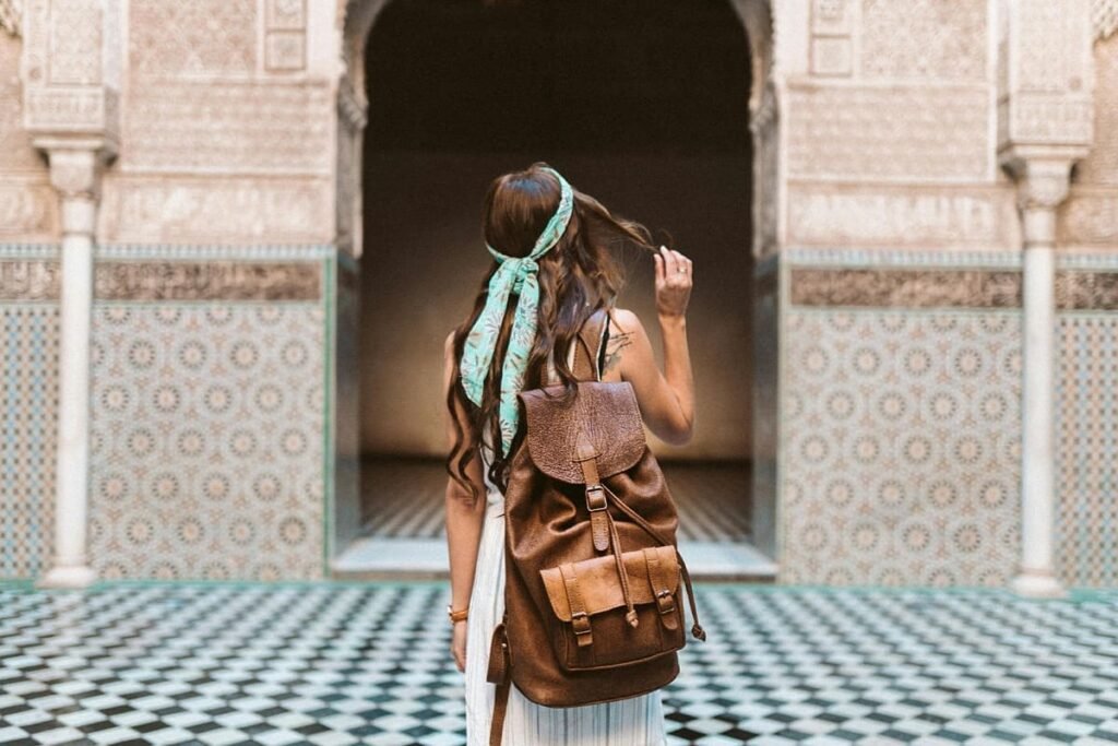 A narrow, bustling alley (souk) inside the Fez medina, depicting visitors exploring shops with traditional Moroccan handicrafts. The image captures the authentic atmosphere and rich culture of Fez’s craft capital.