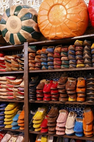 A vibrant display of traditional Moroccan Belgha (slippers) and leather poufs in a Fez market. These handmade leather shoes, known for their pointed toe and high quality, represent the thriving craft of the Khrazz (cobblers).