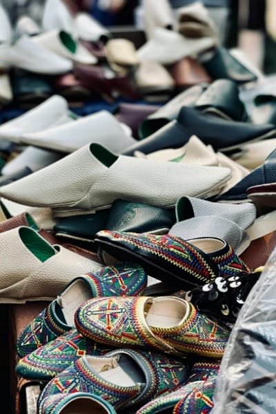 A close-up display of various traditional Moroccan leather slippers, including the Belgha and the intricately embroidered Cherbil. These handmade shoes, crafted by Kharrazine artisans in Fez, are valued for their luxurious, naturally dyed leather and unique designs.