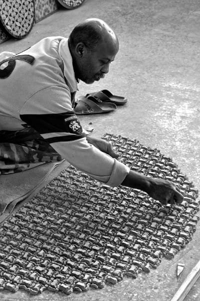 A close-up of a Zellige artisan in Fez manually cutting a glazed tile piece with a hammer and chisel. The process demonstrates the mathematical precision and skill required to create the mesmerizing geometric patterns of traditional Moroccan Zellige.