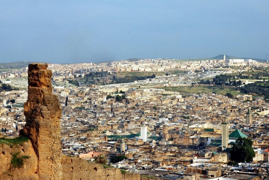 A panoramic view of the historic Fes El Bali medina in Morocco, showcasing the ancient city's dense architecture, minarets, and surrounding hills. The image represents Fez's role as the spiritual heart of Morocco, a center for culture and history.