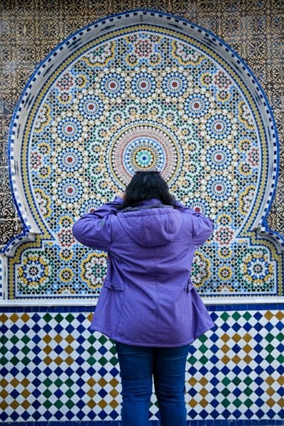 A towering white minaret with a green tiled roof in Fez, representing the city's 1,200 years of history, its role in Islamic scholarship, and the flourishing of craftsmanship. The image captures the architectural excellence that shaped Fez's vibrant culture.