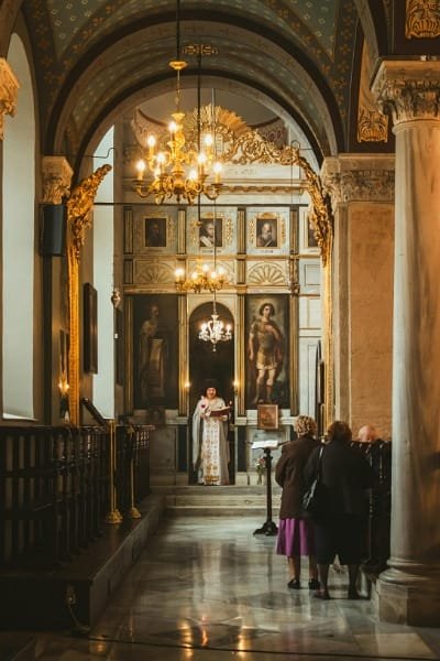 The richly decorated interior of a grand church (similar to St. Peter's Basilica), featuring ornate arches, gold decoration, and religious iconography. Visitors are seen practicing modesty and respect in line with global religious etiquette for visiting sacred Christian sites.