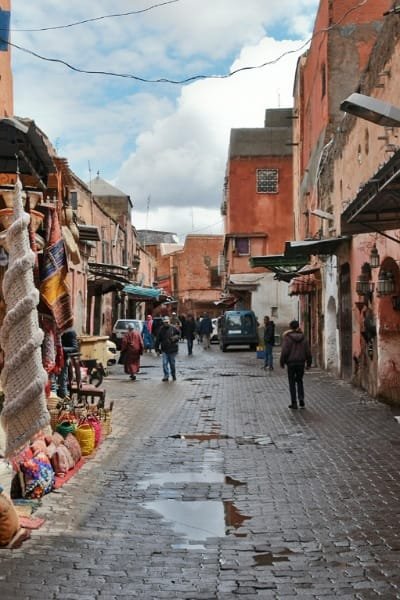 A tourist wearing a brown leather backpack and light clothing stands in a traditional Moroccan riad entrance. This image illustrates smart packing and readiness for the dramatic weather shifts in Fez, ensuring a comfortable and respectful adventure in the medina.