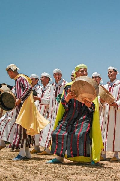 A group of Amazigh (Berber) performers in traditional robes and turbans, dancing and playing drums. Represents the deep indigenous heritage of North Africa and the lively music, such as the mesmerizing rhythms of Ahidous.