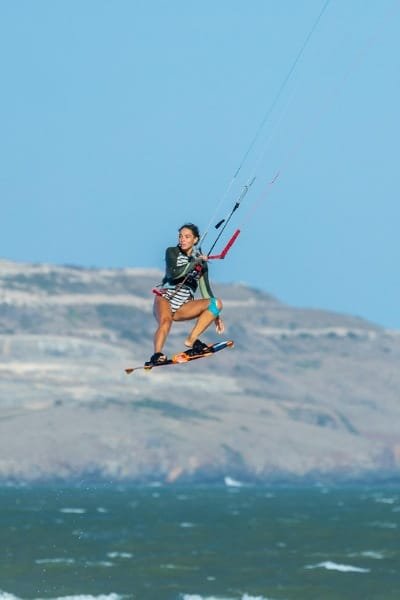 A woman kitesurfer jumping high in the air above the Atlantic Ocean waves. Represents Morocco's diverse coastline and the thrilling water sports available in places like Essaouira, a haven for kitesurfers.