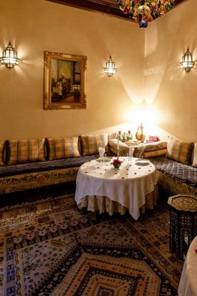 A traditionally decorated Moroccan salon or riad courtyard corner with low seating and a round table. This setting encourages the spontaneous, sincere, and deep conversations over fragrant mint tea that make a trip to Morocco an unforgettable experience.