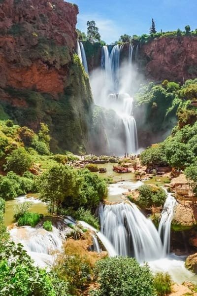 A breathtaking view of the multi-tiered Ouzoud Waterfalls in Morocco, showing the cascade surrounded by lush green vegetation and red cliffs. Represents Morocco's diverse natural scenery and opportunities for day trips and hiking.