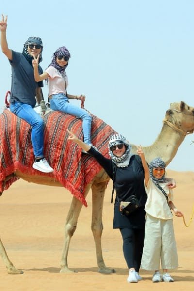 A large group of delighted tourists posing with their guide against a traditional Moroccan wall. The image conveys the fun, vibrant atmosphere and high satisfaction with the service provided in Morocco.