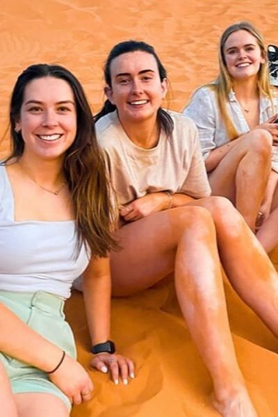 Tourists walking and resting on the vast, golden sand dunes of the Moroccan Sahara. This image promotes popular desert activities like hiking, photography, and exploring the impressive landscape of Merzouga.