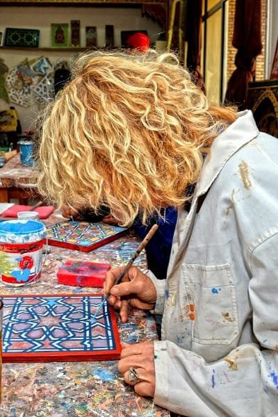 Close-up of an artisan's hands shaping clay on a traditional potter's wheel. This image promotes Moroccan craft workshops where visitors can participate and learn foundational techniques like pottery, rug knotting, or metal embossing.