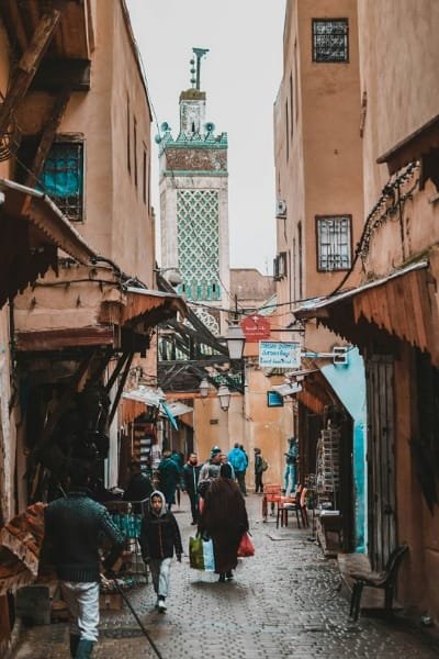 Interior view of a peaceful Zawiya (spiritual lodge) in Fez, featuring traditional Moroccan architecture with ornate arches, red rugs, and a central ablution fountain, representing the historical site of Sidi Ahmed Tijani, founder of the Tijaniyya Sufi order. This site is a living piece of Morocco’s rich Sufi heritage.