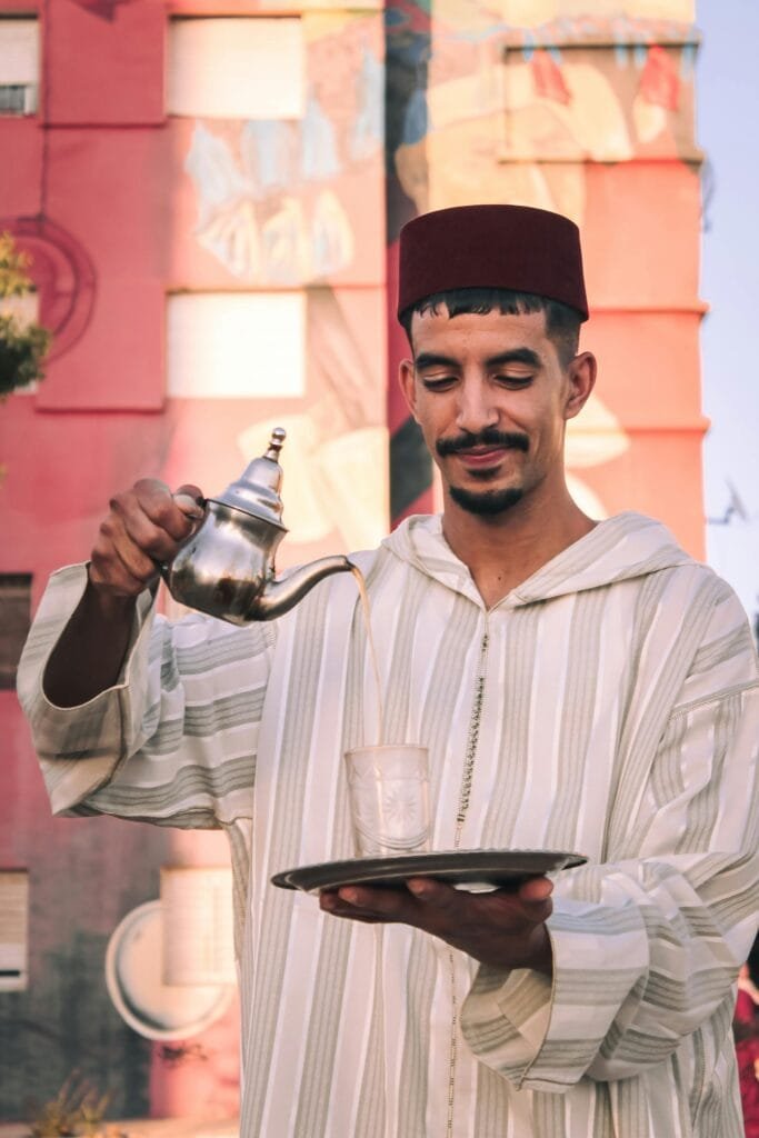 5 Authentic Local Experiences We Recommend Trying in Morocco (Away from the Typical Tourist Spots) 21 In Moroccan culture, the act of serving and sharing mint tea transcends mere refreshment; it is a profound social institution, a timeless ritual steeped in hospitality, friendship, and shared moments of tranquility. To truly connect with the beating heart of Morocco, you must immerse yourself in this essential experience.Imagine stepping into a warm, inviting home or a quiet, traditional café, where the sweet, fragrant aroma of fresh mint tea instantly embraces you. You'll settle down for a traditional tea session, not just as a spectator, but as an honored guest alongside a welcoming Moroccan family or a local storyteller. Watch as the tea is meticulously prepared – fresh mint leaves gently bruised, generous amounts of sugar added, and the amber liquid poured with its characteristic high flourish, creating a delicate foam that signifies perfect aeration.