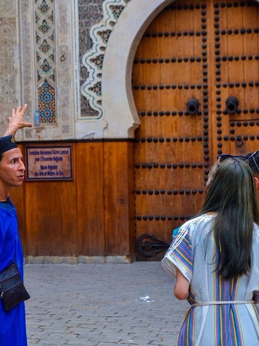Local tour guide in Fes explaining to a tourist in front of a traditional Moroccan door in the Medina.