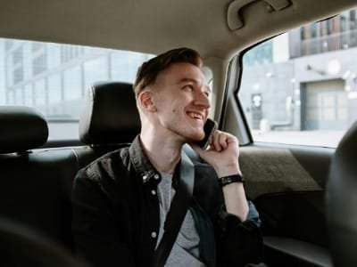 Happy young traveler talking on a mobile phone in the back seat of a private car, promoting flexible and comfortable customized tourist transfer services in Morocco.