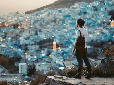 Tourist looking out over the panoramic blue-washed houses of Chefchaouen, promoting a private day trip tour service from Fes to the Blue City, Morocco.