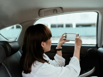Tourist taking a panoramic photo with her phone from the back seat of a private vehicle, promoting a comfortable sightseeing tour of Fes, including the Royal Palace and Borj Sud.