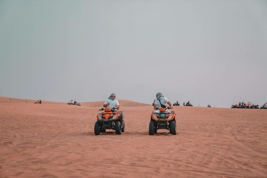 Tourists riding quad bikes (ATVs) over the golden dunes of the Moroccan Sahara Desert.