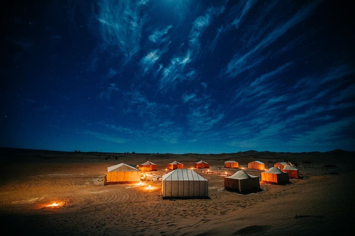 Luxury desert camp illuminated under a starry night sky in the Moroccan Sahara.